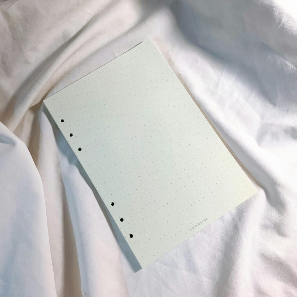 A minimalist dotted notebook page on soft white fabric with natural lighting, perfect for design or writing inspiration.