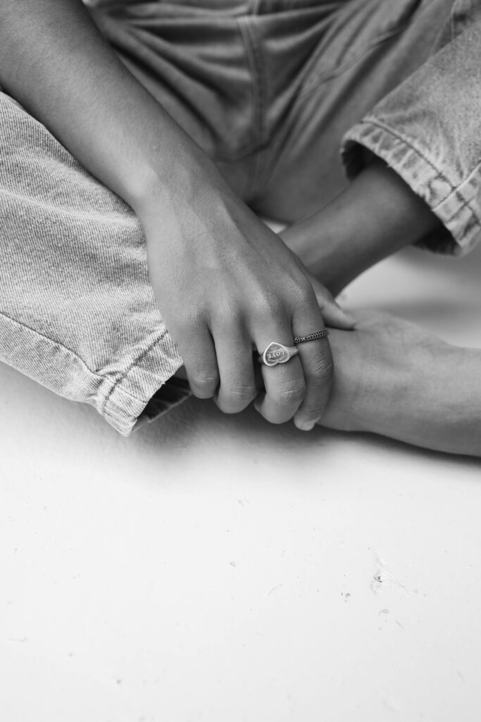 Black and white image showing a hand with rings, jeans, and barefoot on a white surface.