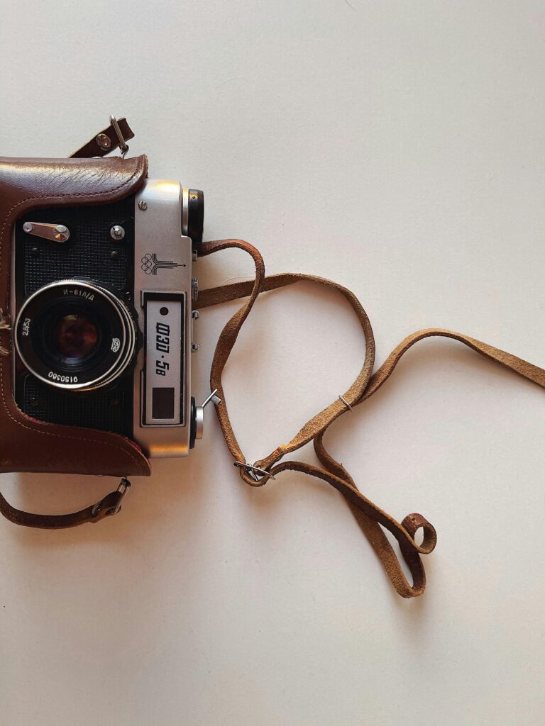 Classic vintage film camera with leather case on a white background, emphasizing nostalgia and photography history.